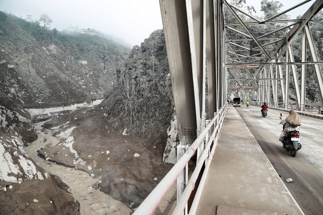 People riding on motorbikes travel past an area covered with volcanic ash following the Mount Semeru volcano eruption in Sumberwuluh, Lumajang, East Java province, Indonesia, on November 21, 2025. (Photo by Dipta Wahyu/Reuters)