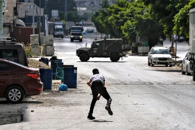A Palestinian youth throws a stone at an Israeli military vehicle during an Israeli army raid in the Balata refugee camp near the West Bank town of Nablus, Saturday, May 13, 2023. the Israeli military raided the Balata refugee camp in the northern city of Nablus, sparking a firefight that killed two Palestinians. (Photo by Majdi Mohammed/AP Photo)