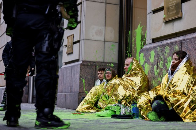 A police officer stands near activists from “Letzte Generation” (Last Generation) sitting in front of a door of the Hotel Adlon, the venue for the World LNG Summit, after green paint was thrown at the door, in Berlin, Germany on December 10, 2024. (Photo by Christian Mang/Reuters)