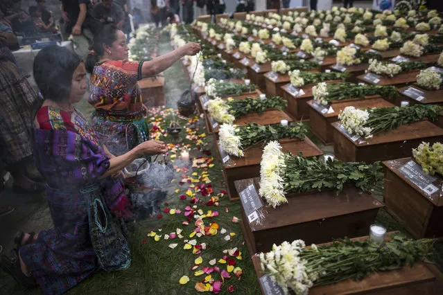 In this June 20, 2018 photo, women burn incense before the remains of 172 unidentified people, who were exhumed from what was once a military camp, during a funeral ceremony in San Juan Comalapa, Guatemala, one day before a formal burial. According to a U.N. report, 97 percent of the crimes committed during Guatemala'a 36 year civil war were perpetrated by the army and paramilitary groups. (Photo by Rodrigo Abd/AP Photo)