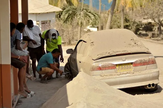 A man fixes a flat tire on a car covered in ash after a series of eruptions from La Soufriere volcano in Orange Hill, Saint Vincent and the Grenadines, April 18, 2021. The tiny eastern Caribbean island of Saint Vincent was blanketed with a thin layer of ash after a volcano spectacularly erupted after decades of inactivity. (Photo by Robertson S. Henry/Reuters)
