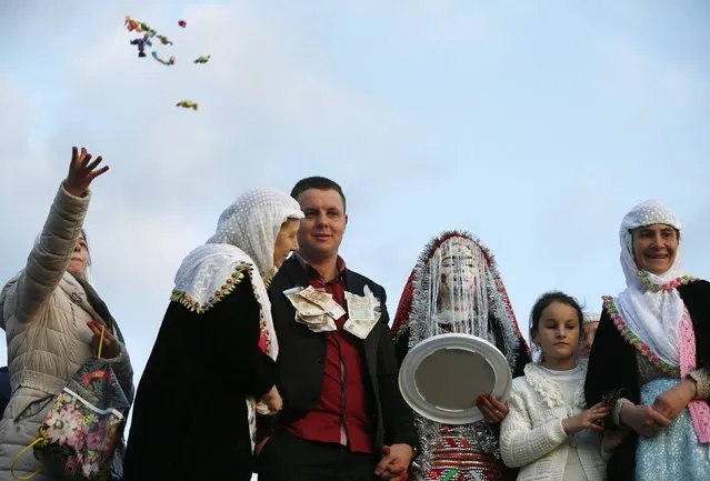 Bulgarian Muslims Azim Liumankov (3rd L) and his bride Fikrie Bindzheva (3rd R) pose in front of their house as a relative throws sweets to the guests during their wedding ceremony in the village of Ribnovo, in the Rhodope Mountains, February 15, 2015. (Photo by Stoyan Nenov/Reuters)