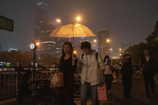 Residents share an umbrella as it starts to rain in Beijing, Friday, August 11, 2023. (Photo by Ng Han Guan/AP Photo)
