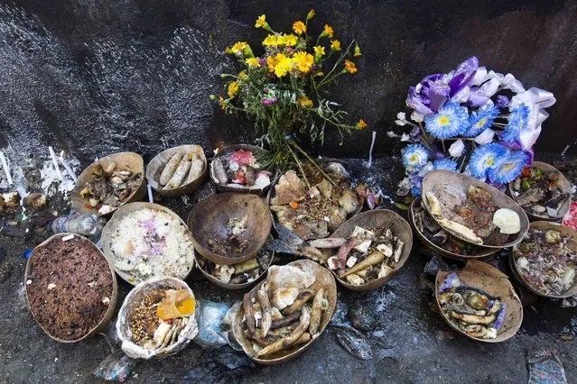 In this November 1, 2018 photo, meals and flowers sits on the ground of Baron Samedi's tomb during the annual Voodoo festival Fete Gede at Cite Soleil Cemetery in Port-au-Prince, Haiti. Accompanied by the priests, the believers, some of them also wearing the loas' clothes, make their annual visit to cemeteries in Port-au-Prince and throughout the country to honor the spirits by offering coffee and meals to the dead loved ones and to the black cross that represents Baron Samedi. (Photo by Dieu Nalio Chery/AP Photo)