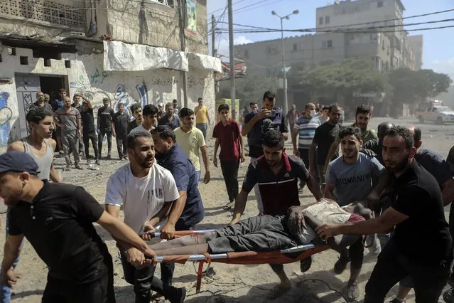 Palestinians carry the  body of a man following Israeli airstrikes hitting buildings, in Gaza City central of the Gaza Strip, Sunday, October 15, 2023. (Photo by Abed Khaled/AP Photo)