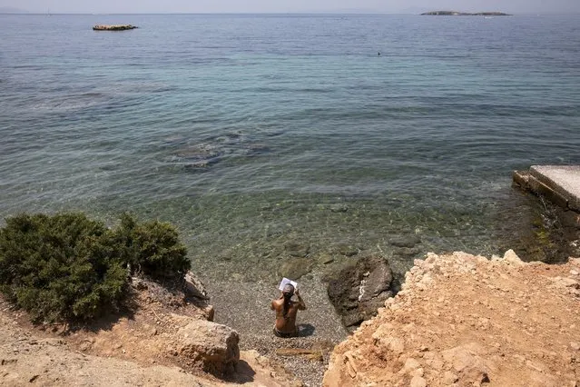A woman reads a book at a beach of Kavouri suburb, southwest of Athens, on Friday, July 30, 2021. Greek authorities ordered additional fire patrols and infrastructure maintenance inspections Friday as the country grappled with a heat wave expected to last more than a week, with temperatures expected to reach 42°C (107.6°F). (Photo by Yorgos Karahalis/AP Photo)