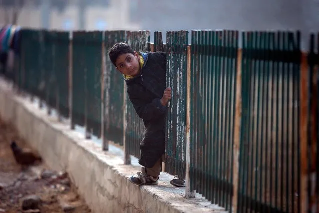 A boy looks on as he passes through an opening in a fence, laid on the boundary of a playground in a neighbourhood in Srinagar December 28, 2016. (Photo by Danish Ismail/Reuters)