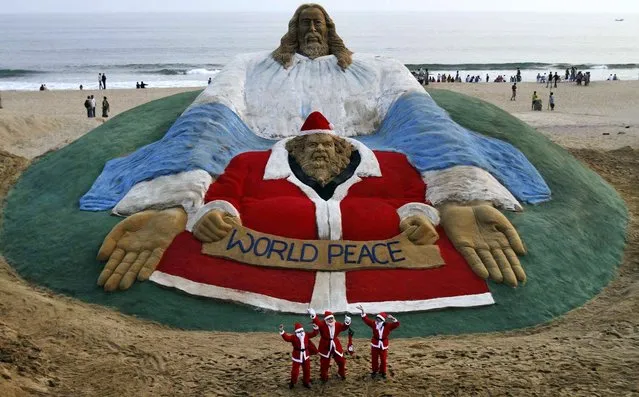 Children dressed as Santa Claus dance in front of a sculpture titled World Peace by sand artist Sudarshan Patnaik at a beach in Puri, India, on December 24, 2013. Though Hindus and Muslims comprise the majority of the population in India, Christmas is celebrated with much fanfare. (Photo by Biswaranjan Rout/Associated Press)