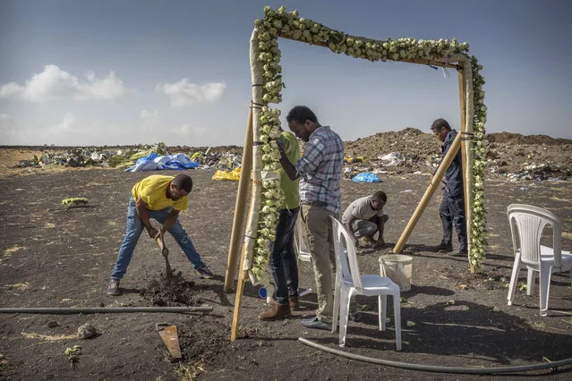 Workers erect floral installations at the scene where the Ethiopian Airlines Boeing 737 Max 8 crashed shortly after takeoff on Sunday killing all 157 on board, near Bishoftu, or Debre Zeit, south of Addis Ababa, in Ethiopia Wednesday, March 13, 2019. Much of the world, including the entire European Union, has grounded the Boeing jetliner involved in the Ethiopian Airlines crash or banned it from their airspace, leaving the United States as one of the few remaining operators of the plane involved in two deadly accidents in just five months. (Photo by Mulugeta Ayene/AP Photo)