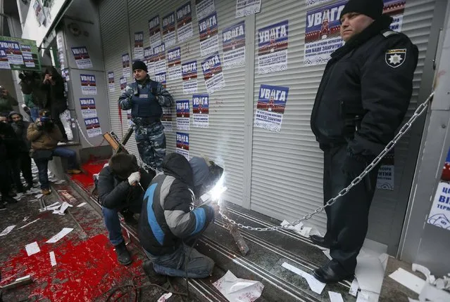 Members of the “Azov” civil corp install a steel chain during a protest outside the central branch of Sberbank in Kiev, Ukraine, February 2, 2017. The stickers read “Attention. This is a bank of the aggressor state. It will be closed. Immediately take back your money”. (Photo by Valentyn Ogirenko/Reuters)