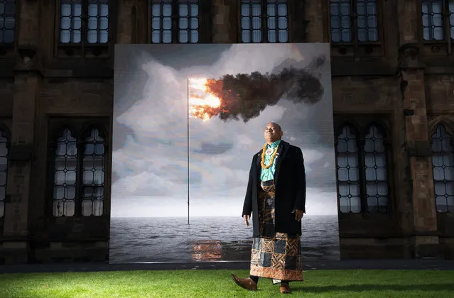 Tongan activist Uili Lousi stands alongside “Flare Oceania 2021”, created by artist John Gerrard, a real-time moving image showing a simulation of the seas around Tonga with the flag/flare embedded in it, displayed on the South Facade of the University of Glasgow to mark Ocean Day, at the COP26 climate summit, in Glasgow, Scotland, Friday, November 5, 2021. (Photo by Jane Barlow/PA Wire via AP Photo)