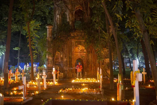 Burning candles illuminate graves as a Bangladeshi man observes a contemplative moment on All Souls' Day at the Dhaka Christian Cemetery at Wari in Dhaka, Bangladesh, 02 November 2021. People on All Saints Day and All Souls Day pay respect to deceased relatives and loved ones by placing flowers on their tombs or maintaining their graves and lighting candles. (Photo by Monirul Alam/EPA/EFE)