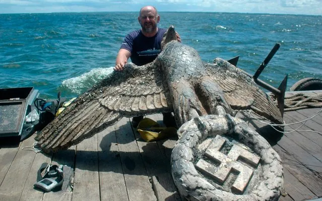 In this handout photo taken on February 13, 2006, a man poses with the eagle from the stern of WW2 German battleship “Admiral Graf Spee”, scuttled on December 17, 1939 off the coast of Montevideo, after being recovered from the depths of the estuary. The Uruguayan Justice ordered the sale of a bronze sculpture of a Nazi eagle with a swastika recovered 13 years ago from the stern of WW2 German battleship Graf Spee, scuttled 17 December 1939 in front of the city port, after a fierce battle with three British battlecruisers in what is known as “The battle of the River Plate”. (Photo by Alfredo Etchegaray/AFP Photo/HO)
