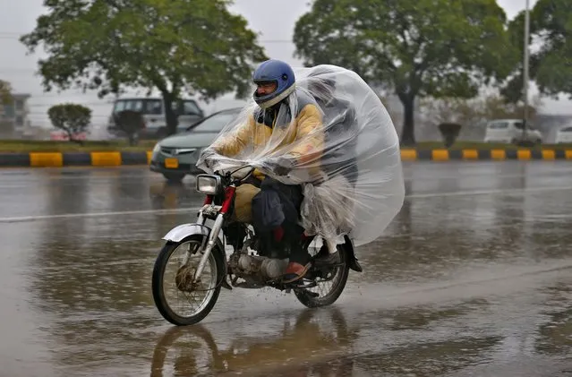 A motorcyclist covers themselves with plastic sheet to protect from rain at a highway, in Islamabad, Pakistan, Friday, January 7, 2022. (Photo by Anjum Naveed/AP Photo)