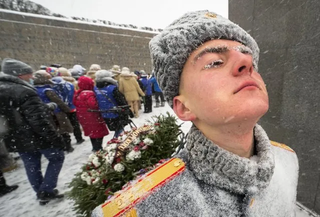 A honour guard soldier stands in snowfall as people walk to the Motherland monument to place flowers and wreaths at the Piskaryovskoye Cemetery where most of the Leningrad Siege victims were buried during World War II, in St.Petersburg, Russia, Thursday, January 27, 2022. People gathered to mark the 78th anniversary of the battle that lifted the Siege of Leningrad. The Nazi German and Finnish siege and blockade of Leningrad, now known as St. Petersburg, was broken on Jan. 18, 1943 but finally lifted Jan. 27, 1944. More than 1 million people died mainly from starvation during the 900-day siege. (Photo by Dmitri Lovetsky/AP Photo)