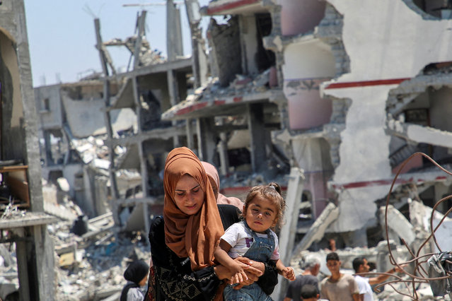 A Palestinian woman holds her daughter as she walks past the rubble of houses destroyed during the Israeli military offensive, amid Israel-Hamas conflict, in Khan Younis in the southern Gaza Strip on July 10, 2024. (Photo by Hatem Khaled/Reuters)