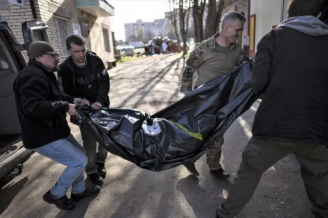 Volunteers carry the body of a man killed during the war to a refrigerated container in Bucha, in the outskirts of Kyiv, Ukraine, Thursday April 14, 2022. (Photo by Rodrigo Abd/AP Photo)