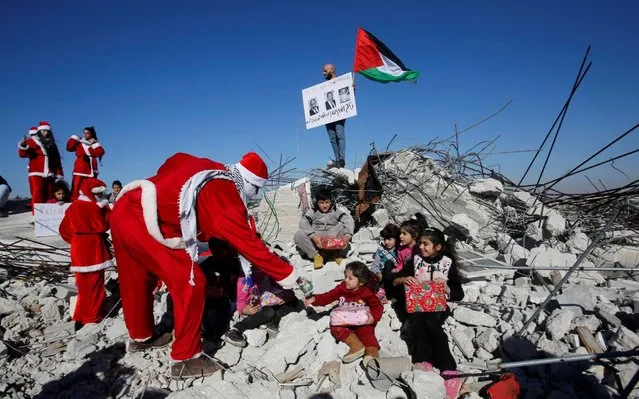 A demonstrator dressed as Santa Claus hands out gifts to children sitting on the remains of a demolished Palestinian house during an anti-Israel protest, in Bethlehem in the Israeli-occupied West Bank om December 23, 2019. (Photo by Mussa Qawasma/Reuters)