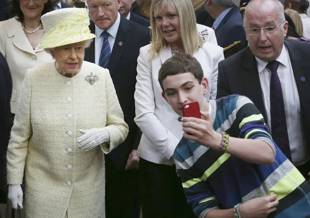 A local youth takes a selfie photograph in front of Queen Elizabeth II during a visit to St George's indoor market on  in Belfast Tuesday June 24, 2014. The Queen is on a 3 day visit to Northern Ireland . (Photo by Peter Macdiarmid/AP Photo)