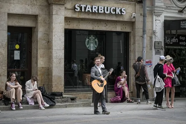 A young man plays guitar as other applicants to the Moscow Art Theatre School wait for their turn at an admission exam gather in front of a closed due to sanctions Starbucks street cafe, in Moscow, Russia, Thursday, June 2, 2022. (Photo by Alexander Zemlianichenko/AP Photo)