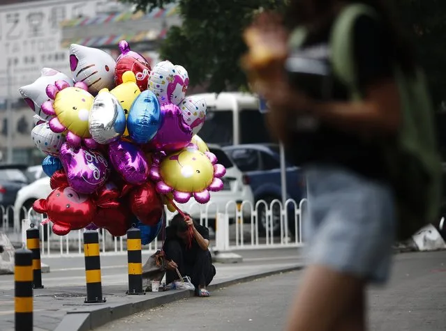 A vendor eats by the side of a street while holding on to balloons at a shopping district in Beijing July 17, 2014. (Photo by Kim Kyung-Hoon/Reuters)