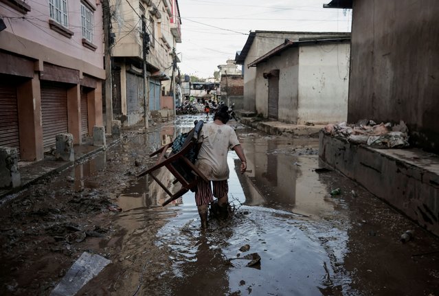 A woman carrying a chair walks along a muddy street as the floodwater recedes from a residential area that was flooded by the overflowing Bagmati River following heavy rains in Kathmandu, Nepal on September 29, 2024. (Photo by Navesh Chitrakar/Reuters)