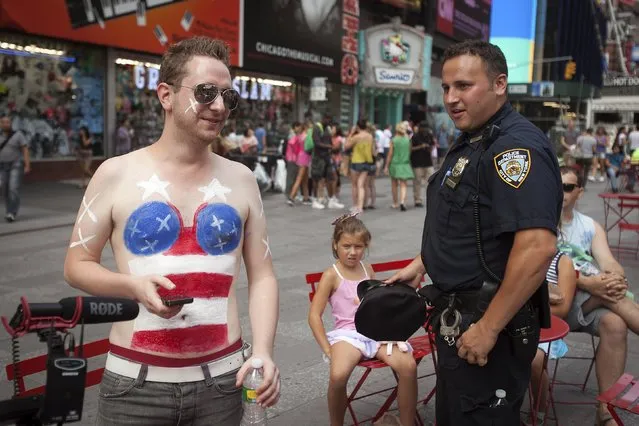 A policeman talks to Greg Burmeister of Coed Media as he prepares to parody the women who pose for tips wearing only body paint and underwear in Times Square in New York, August 19, 2015. (Photo by Carlo Allegri/Reuters)