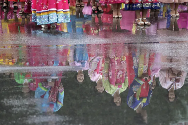 University students dressed in their traditional Korean dresses are seen in a reflection from a puddle as they wait in the rain for the start of a mass dance on Thursday, July 27, 2017, in Pyongyang, North Korea as part of celebrations for the 64th anniversary of the armistice that ended the Korean War. (Photo by Wong Maye-E/AP Photo)