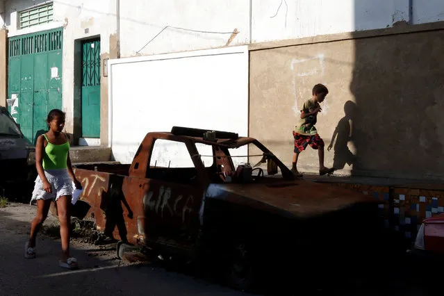 A boy walks past a rusty old car in a low income neighborhood in Caracas, Venezuela July 9, 2016. (Photo by Carlos Jasso/Reuters)
