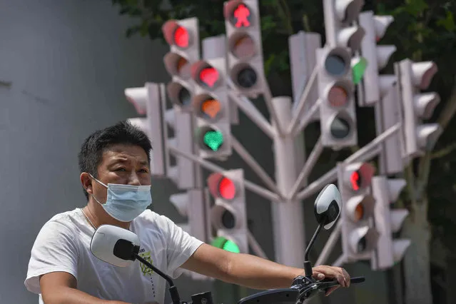 A man wearing a face mask rides past a creative traffic lights on display along a street in Beijing, Sunday, July 24, 2022. (Photo by Andy Wong/AP Photo)