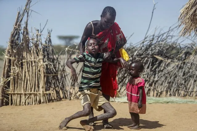 A mother helps her malnourished son stand after he collapsed near their hut in the village of Lomoputh in northern Kenya, May 12, 2022. Russian, French and American leaders are crisscrossing Africa in July 2022, to win support for their positions on the war in Ukraine, an intense competition for influence the continent has not seen since the Cold War. (Photo by Brian Inganga/AP Photo/File)