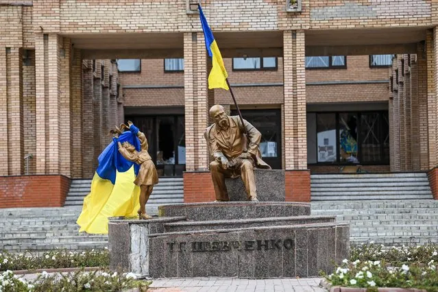 A photograph taken on September 10, 2022, shows Ukrainian flags placed on statues in a square in Balakliya, Kharkiv region, amid the Russian invasion of Ukraine. (Photo by Juan Barreto/AFP Photo)