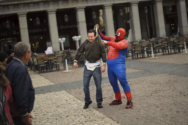 A man dressed as  comic super-hero Spiderman performs with a tourist while they pose for pictures in the Plaza Mayor, in Madrid, Monday, April 30, 2012. (Photo by Daniel Ochoa de Olza/AP Photo)