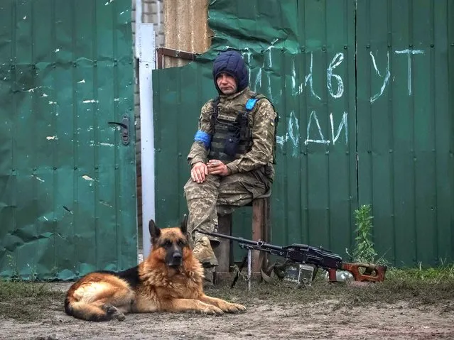 Ukrainian serviceman patrols an area as a dog sits near by, as Russia's attack on Ukraine continues, in the town of Izium, recently liberated by Ukrainian Armed Forces, in Kharkiv region, Ukraine on September 14, 2022. (Photo by Gleb Garanich/Reuters)