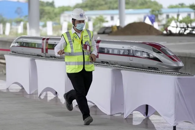 A worker runs past a model of a high-speed train displayed at the Jakarta-Bandung Fast Railway station in Tegalluar, West Java, Indonesia, Thursday, October 13, 2022. The 142-kilometer (88-mile) high-speed railway worth $5.5 billion is being constructed by PT Kereta Cepat Indonesia-China, a joint venture between an Indonesian consortium of four state-owned companies and China Railway International Co. Ltd. The joint venture says the trains that will be the fastest in Southeast Asia. (Photo by Dita Alangkara/AP Photo)