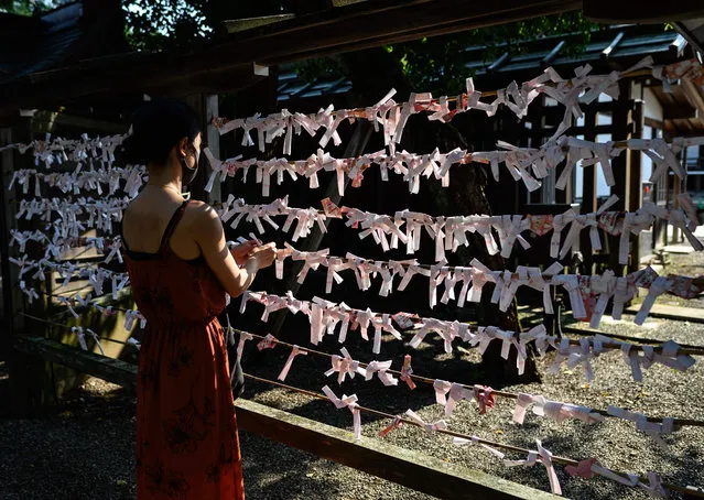 A visitor attaches a fortune telling slip of paper, also known as “omikuji”, to a display during her visit to Yasukuni Shrine in Tokyo on August 14, 2020, one day before the 75th anniversary of Japan's surrender in World War II. (Photo by Philip Fong/AFP Photo)