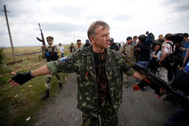 An armed pro-Russian separatist stands guard as monitors from the Organization for Security and Cooperation in Europe (OSCE) and a team of Malaysian air crash investigators inspect the crash site of Malaysia Airlines Flight MH17, near the village of Hrabove (Grabovo), Donetsk region July 22, 2014. (Photo by Maxim Zmeyev/Reuters)