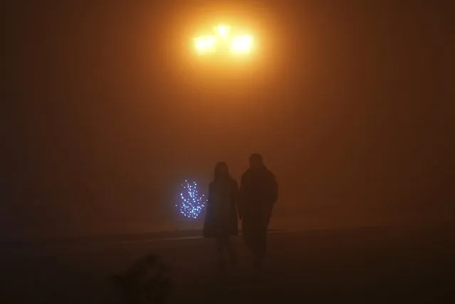 A couple walk in the fog along the street in a poorly lit Stepanakert, the capital of the separatist region of Nagorno-Karabakh, also known as Artsakh, on Thursday, December 15, 2022. In the region have been periodic shutoffs of gas and electricity to the region during the dispute. Protesters claiming to be ecological activists have blocked the only road leading from Armenia to Nagorno-Karabakh for more than a month, leading to increasing food shortages. (Photo by Edgar Harutyunyan/PAN Photo via AP Photo)
