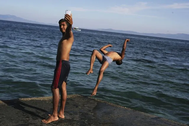 A Bangladeshi migrant takes a selfie as his friend jumps in the sea near the port of Mytilini on the northeastern Greek island of Lesbos, Greece, on Friday October 7, 2016. More than a million migrants and refugees crossed through Greece and on to other EU countries since the start of 2016, while over 60,000 have been stranded in the country since the EU-Turkey deal took effect and the Balkan transit route north was closed. (Photo by Petros Giannakouris/AP Photo)