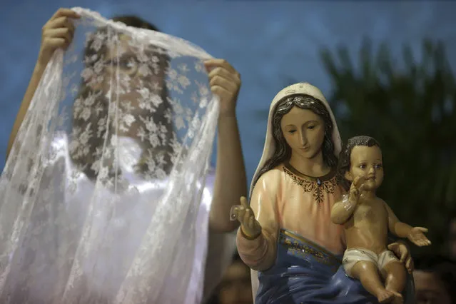 In this October 7, 2016 photo, a girl prepares to place a veil on a statue of Our Lady of the Rosary during the annual Afro-Christian Congada celebration in Catalao, Goias state, Brazil. According to local legend, the ritual was first performed by Black slaves in the 1800s in Brazil where the Catholic icon, Our Lady of the Rosary, is associated with the African divinity Yemanja, or Sea Mother. (Photo by Eraldo Peres/AP Photo)