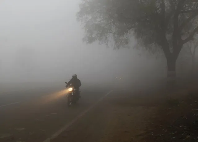 A man rides a motorcycle through dense fog on a road during winter morning in the northern Indian city of Allahabad December 19, 2014. (Photo by Jitendra Prakash/Reuters)