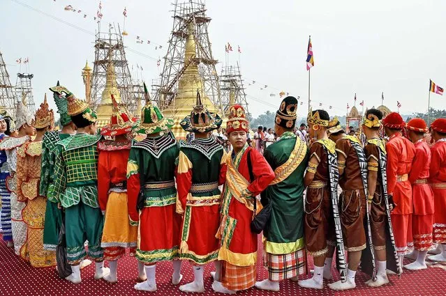 People dressed in traditional religious clothing gather for a Buddhist ceremony in which an auspicious golden umbrella is placed at the top of a pagoda, donated by Karen state Border Guard Forces chief Saw Chit Thu, at Pyi Thar Lin Aye pagoda in Hlaingbwe township in Karen state on March 5, 2023. (Photo by AFP Photo/Stringer)