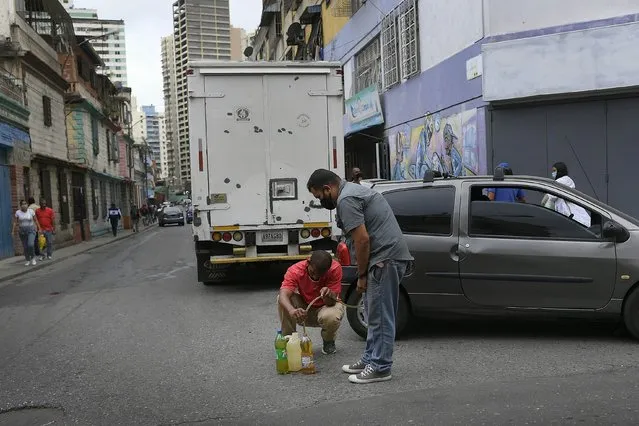 Men siphon from a car gasoline that they will store and then return to the gas station to fill up again, in the San Juan neighborhood of Caracas, Venezuela, Tuesday, January 19, 2021, amid the new coronavirus pandemic. Filling stations will only fill up car and motorcycle tanks, but not containers to avoid people from storing gasoline. (Photo by Matias Delacroix/AP Photo)