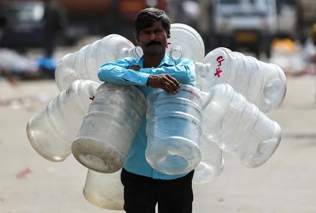 A man walks with empty water bottles around his neck to fill water to be sold for drinking in New Delhi, India on May 18, 2023. (Photo by Anushree Fadnavis/Reuters)