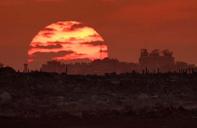 In this picture taken from a position on the Israeli border with the Gaza Strip, the sun sets behind destroyed buildings in the Palestinian territory on August 7, 2025. (Photo by Jack Guez/AFP Photo)