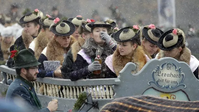 Women wearing the traditional costumes of the region drink liqueur as they are sitting in a horse-drawn carriage during the traditional Leonhardi pilgrimage in Bad Toelz, southern Germany, Monday, November 7, 2016. The annual pilgrimage honors St. Leonhard, patron saint of the highland farmers for horses and livestock. (Photo by Matthias Schrader/AP Photo)
