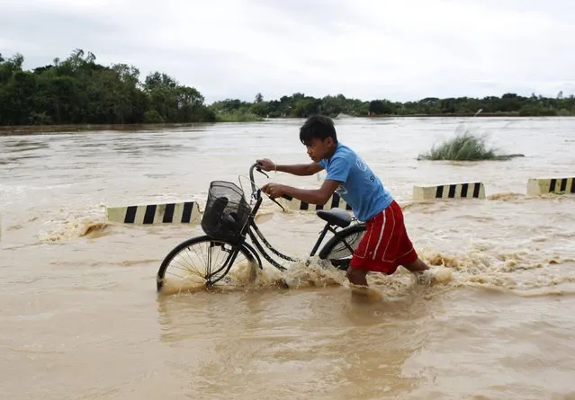 A boy pushes his bicycle through a flooded road after heavy rain at Candaba town, Pampanga province, north of Manila, December 17, 2015. (Photo by Czar Dancel/Reuters)