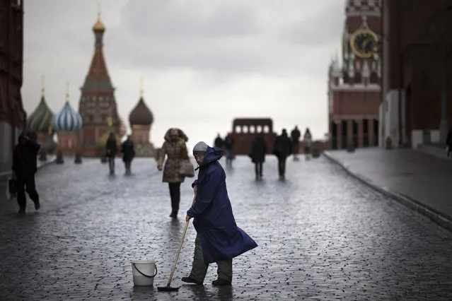 A street worker cleans paving stones in Red Square with St. Basil's Cathedral, left, Lenin Mausoleum,  center, and the Spasskaya Tower, right, in Moscow, Russia, Tuesday, December 22, 2015. It's usually the cold that's bitter in Moscow in December, but this year it's the humor that bites during an unusual warm spell and temperatures climbed as high as 10 degrees Celsius (50 degrees Fahrenheit). (Photo by Alexander Zemlianichenko/AP Photo)