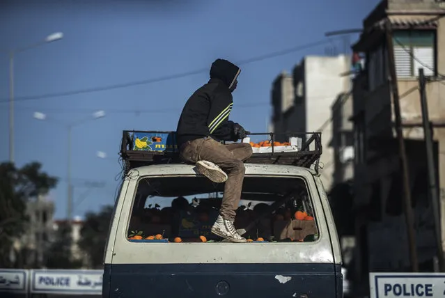 A Palestinian man sits on top of a vehicle loaded with boxes of oranges while passing a police checkpoint in the southern Gaza Strip, Monday, February 1, 2021. (Photo by Khalil Hamra/AP Photo)