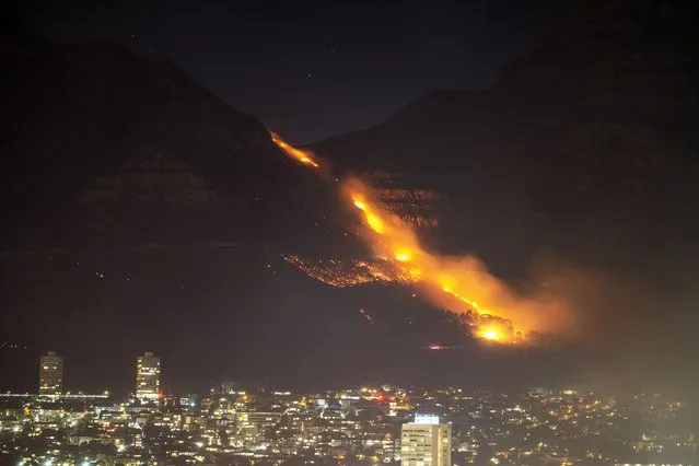 Residential neighborhoods are lit by raging fires in Cape Town, South Africa, Monday, April 19, 2021. Residents are being evacuated from Cape Town neighborhoods after a huge fire spreading on the slopes of the city's famed Table Mountain was fanned by strong winds overnight and threatened houses. (Photo by Jerome Delay/AP Photo)
